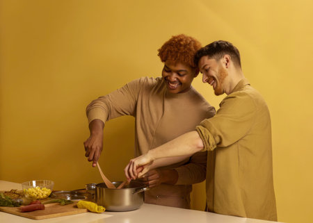 Two smiling individuals share a moment of culinary delight in a bright yellow kitchen, preparing a meal with vegetables and cooking utensils. The image evokes warmth, friendship, and the pleasure of shared cooking.の素材