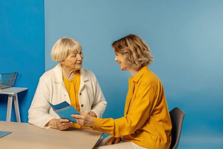 Mature female doctor talking to senior woman patient while sitting at tableの素材