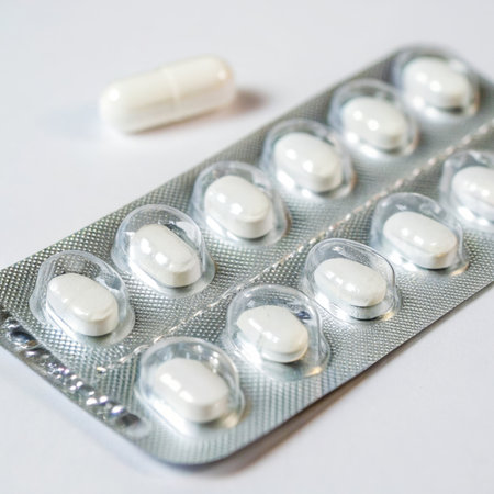 A close-up shot showcases a transparent blister pack meticulously filled with multiple white pills, arranged within individual compartments. The blister pack rests upon a light-colored surface with a subtle fabric or plastic texture. A solitary white pill lies adjacent to the pack, slightly out of focus. The pills themselves are smooth, rounded, and have a reflective surface, suggesting a hard gelatin or similar material. The lighting is soft and even, emphasizing the pack's transparency without harsh shadows. This image evokes a feeling of cleanliness, organization, and precisionの素材