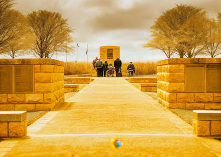 A group of people stand respectfully at the foot of a stone monument, bathed in soft, diffused light. The scene evokes a sense of quiet contemplation and reverence, suitable for memorial or commemorative projects.の素材