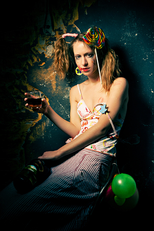 Disheveled clown sitting drinking alcohol with a lollipop in her hair.の写真素材