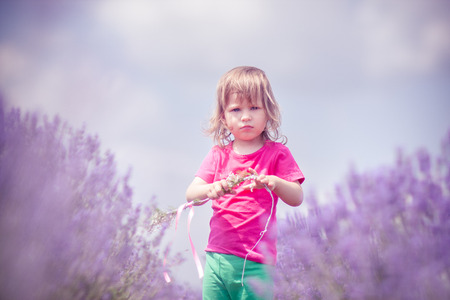 Little blone girl on the field of lavender with little ouquet with pink ribbon.の写真素材