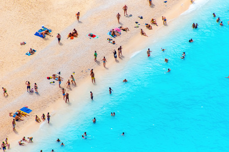 People on the beach sunbathe and bathe in the clear water of Zakynthos, Navaggio