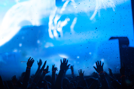 Silhouette of raised hands spectators on background beautiful light show. Blue background, large screen monitor, confetti.の写真素材
