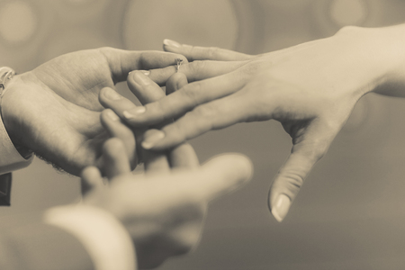 The groom puts a wedding ring on bride's finger, gently. Macro frame of hands newlyweds in sepia tone.の写真素材