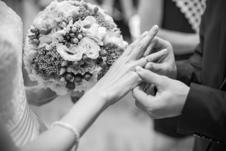 Husband puts a wedding ring on brides finger. Bride with wedding bouquet. Photo in black&white colors.の写真素材