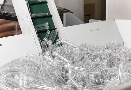 Pile of plastic flasks prepared for bottle making on conveyor on a factory.
