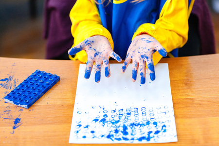 Crop unrecognizable child standing at table and making blue colored stains on paper.の写真素材