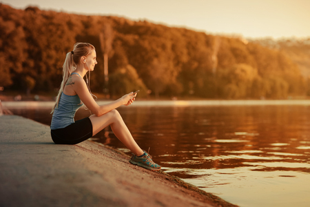Active and beautiful girl in a blue sports t-shirt, listening to music via the player in the mobile phone touch.の写真素材