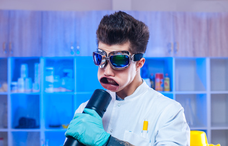 Young scientist in glasses having fun and blowing with wind machine to face in the lab.