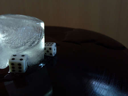two dice and a cold block of ice with bubbles are placed on a black vinyl record in an abstract...