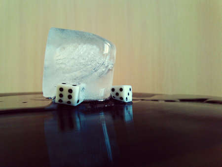 a pair of dice and a cold piece of ice with bubbles are lying on an old vinyl record in a retro...