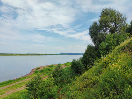 green hillside near the river bank against a blue sky with clouds