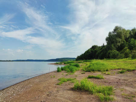 blue cloudy sky over green river bank on sunny dayの写真素材