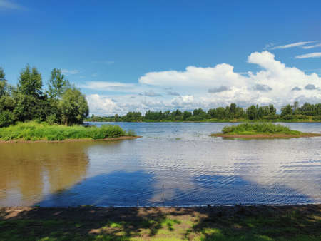 green islets on the river against the background of blue sky with clouds on a sunny day