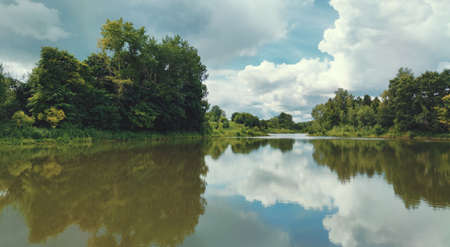 reflection of clouds and trees on the water surface of the pond