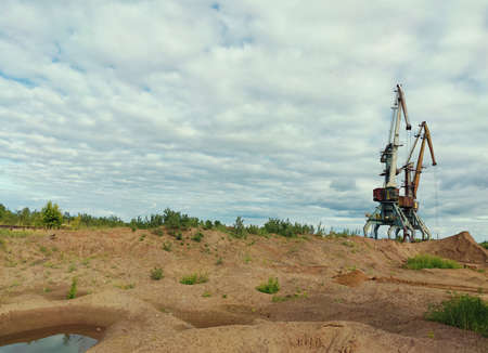 two huge cranes on a sand quarry against a blue cloudy sky