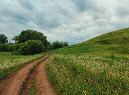 cloudy sky before rain over a country road near a green hillsideの写真素材