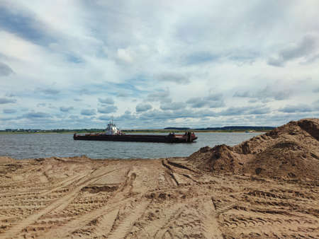 barge near the sandy bank of the river against the background of a blue cloudy sky on a sunny dayの写真素材