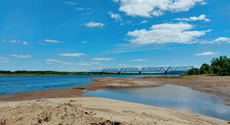 beautiful panorama on the sandy bank of the river near the bridge on a background of blue sky with...