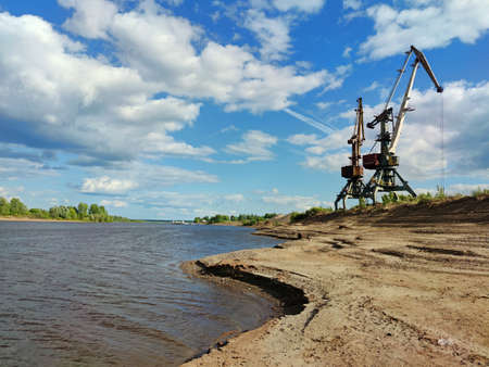 two river cranes on the sandy bank of the river against a beautiful blue sky with clouds