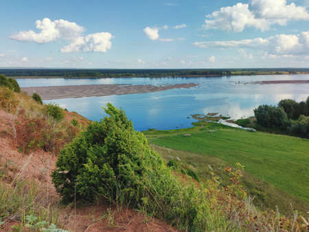 mountainside on the background of a river with a sandy island and a blue sky with clouds