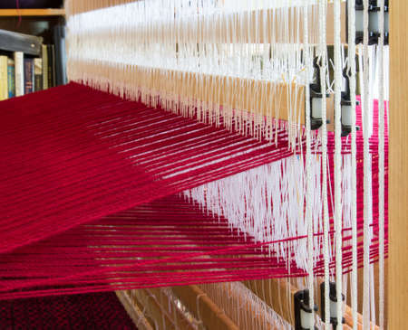 The white string heddles separate the red warp threads on this loomの写真素材