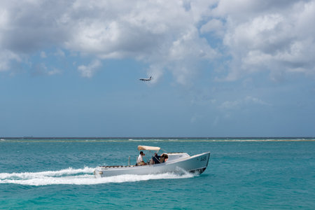 Classic boat in touristic route in the outskirts of the Oranjestad coast, with plane bottom preparing to land. Oranjestad. Aruba February 23, 2019のeditorial素材