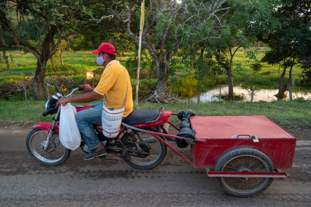 Man on a motorcycle towing a small trailer behind a rural road in the department of Cordoba....
