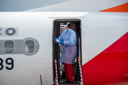 Flight attendant at the door of a plane of the avianca airline with a face mask for the protection...