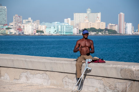 Athletic man with disability in one leg sitting on a wall by the sea waving at the camera on a sunny day. Havana. Cuba. May 12, 2015のeditorial素材