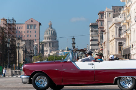Red and white convertible car on a sunny day in an avenue of old Havana with the capitol and the old city in the background on May 12, 2015のeditorial素材