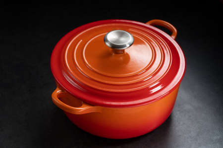 Red ceramic cooking pot with lid on black background. Copy space.の写真素材