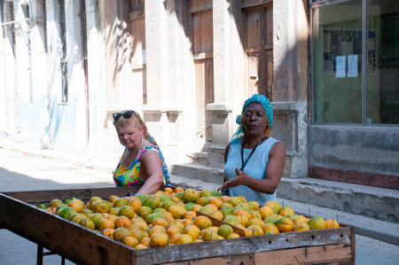 Two women in front of a cart of mangoes for sale on a street in old Havana. Havana. Cuba. May 12, 2015.のeditorial素材