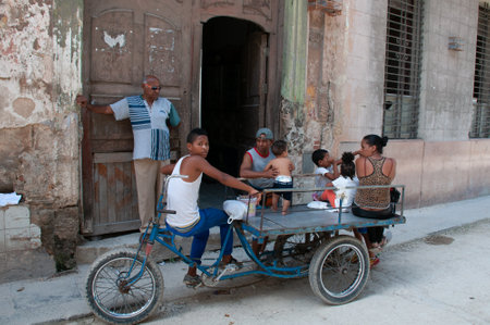 Family sitting on a tricycle at the door of an old facade in Old Havana. Havana. Cuba. May 14, 2015.のeditorial素材