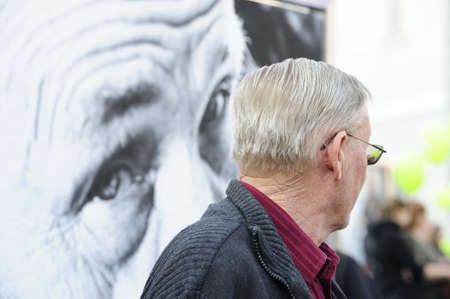 Old man standing alone in front of a portrait