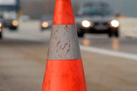 Road safety: traffic cone in front and car headlights in the back