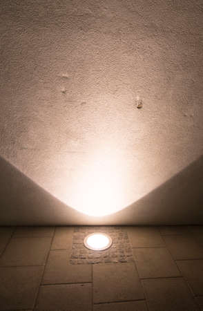 a halogen light spot in the pavement illuminates a wallの写真素材