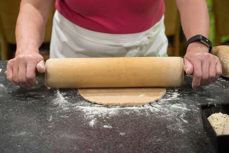 woman using a rolling pin forming bread dough in a kitchen