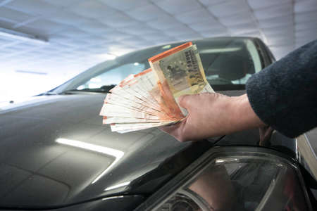 holding a bunch of bank notes in front of a car, car expenses