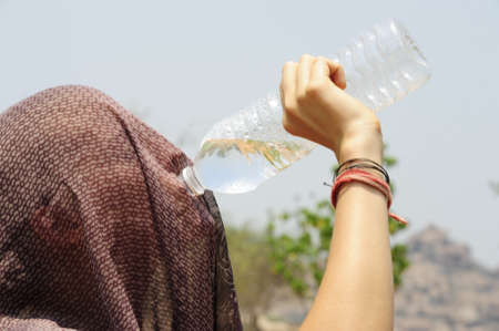 woman with covered head drinking water from a plastic bottle, symbol for isolation, human psyche