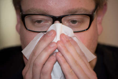 man with glasses blows his nose with a handkerchiefの写真素材