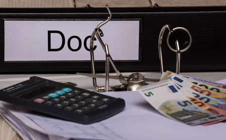 black folder with a DOC sign, calculator and money on the deskの写真素材