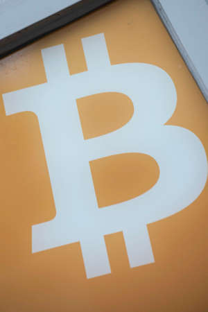 white bitcoin sign on an orange background at a shop