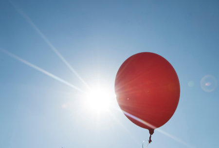 red balloon and blue sky background with sun, symbol for joy and happinessの写真素材