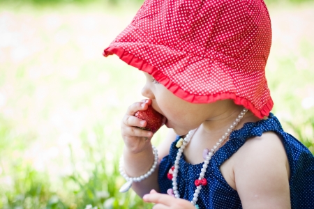 cute baby girl is eating strawberries in summerの写真素材