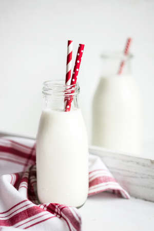 Milk jar with red striped straws on white wooden backgroundの写真素材
