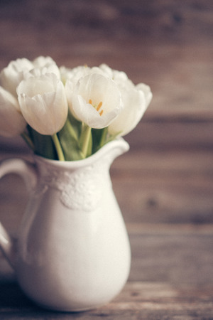 White tulips in a vase in pastel colors on rustic backgroundの写真素材