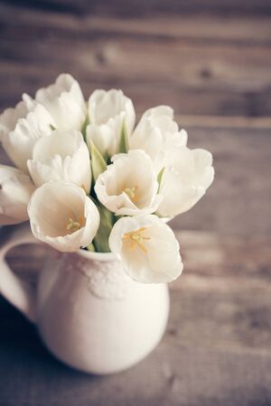 White tulips in a vase in pastel colors on rustic backgroundの写真素材
