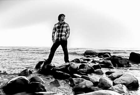 American Teenager  Young male poses standing on rocks with Lake Huron as a backdrop 